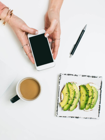 Overhead shot of coffee, avocado and a hand holding an iPhone